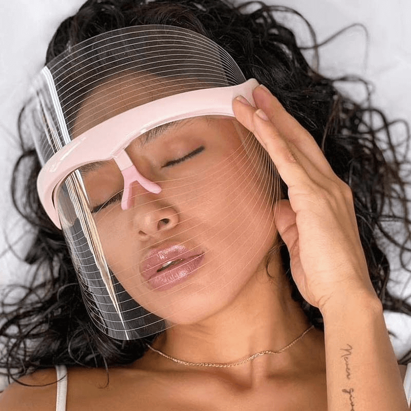 Woman relaxing with a transparent face shield, showcasing beauty care and skincare routine concepts.